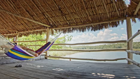 slow motion of man having a nap on hammock inside a hut in chunyaxche, quintana roo, mexico. wide panning shot.