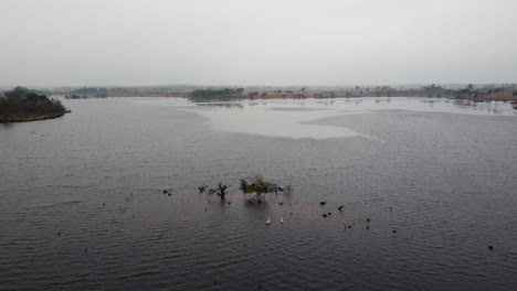 Pequeña-Isla-En-Medio-Del-Lago,-Tiro-Aéreo-Ascendente-En-Un-Día-Brumoso-Y-Cambiante