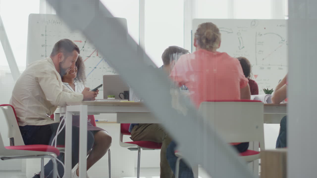 a través de la gente de vidrio sentada en la mesa de la sala de juntas, colegas conociendo oficinas modernas.