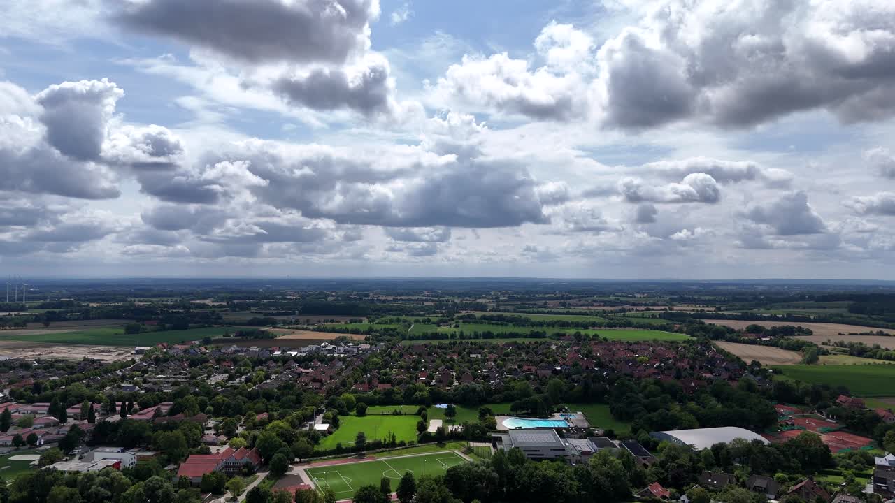 Aerial wide angle of small American town in rural area with clouds at sky. Soccer field and public swimming bath in summer. Wide shot. Farm fields of countryside in distance. Kentucky, USA