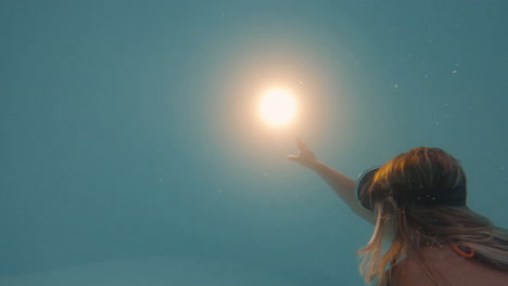 cinematic shot of a woman swimming towards a bright light underwater while wearing an orange bikini and vintage diving goggles shot in 4k, 120 fps, slow motion