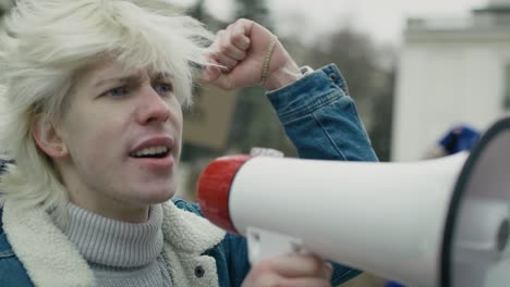 close up caucasian woman  screaming through megaphone in front and group of people manifesting  in the background.