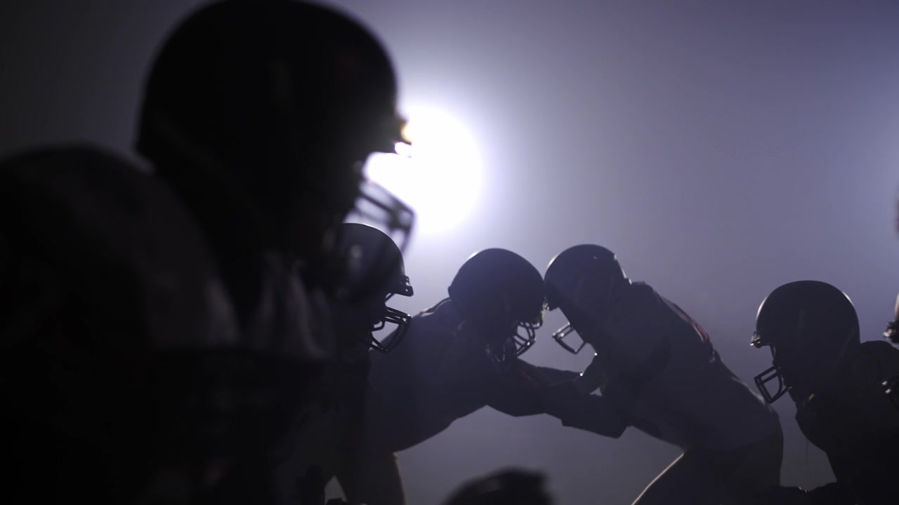 Joueurs de football américain en pleine mêlée sous les lumières du stade