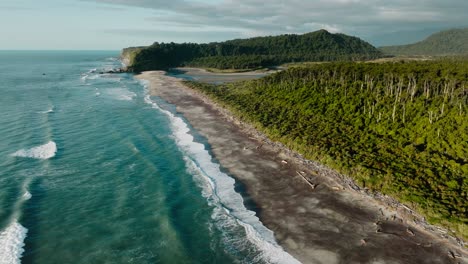 wild and rugged aerial view of bruce bay tree covered landscape, driftwood covered beach, river mouth, and the tasman sea in south westland, new zealand aotearoa