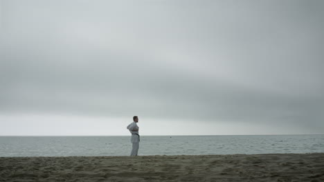 active sportsman practicing martial arts on beach. man training karate outside.