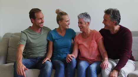 happy caucasian couple and senior parents or in laws sitting on couch talking and smiling to camera