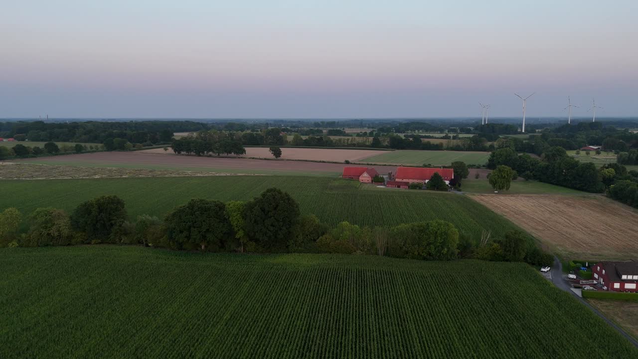 Typisk tysk bondegård med røde mursten og orange tagsten i landlige omgivelser i en stille forstad. Morgengry. Vindmøller i baggrunden. Bredt luftfoto fremad. Dyrkede marker