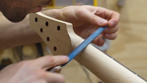 close-up view of a young luthier shaping guitar's neck with rasp, removing roughness and bumps