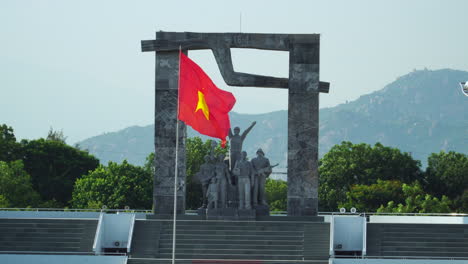 Static-shot-of-Vietnamese-flag-with-monument-in-background,-Phan-Rang-center