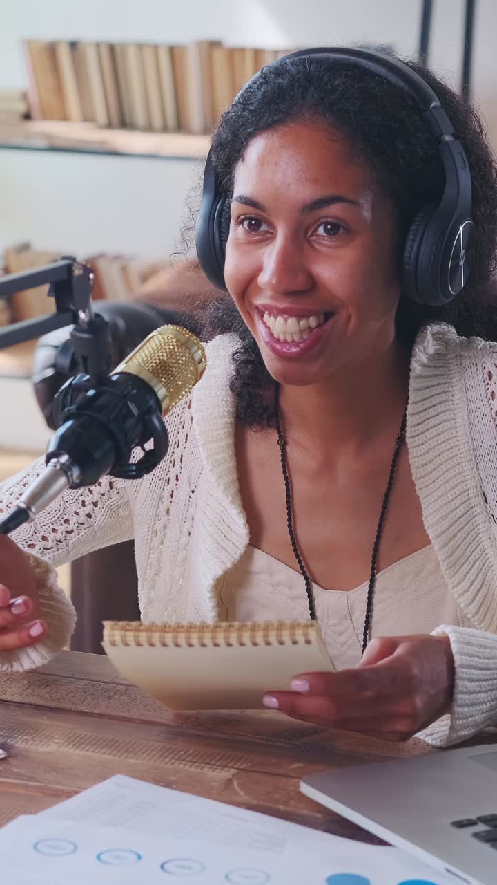 Giovane conduttrice radiofonica afroamericana trasmette seduta al tavolo con il laptop.