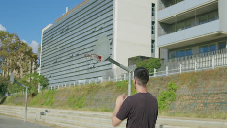 Tiro-Medio-En-Cámara-Lenta-De-Un-Tiro-De-Tres-Punteros-Y-Canasta-De-Un-Joven-Caucásico-En-Una-Cancha-De-Baloncesto-De-La-Calle-En-Barcelona,-España