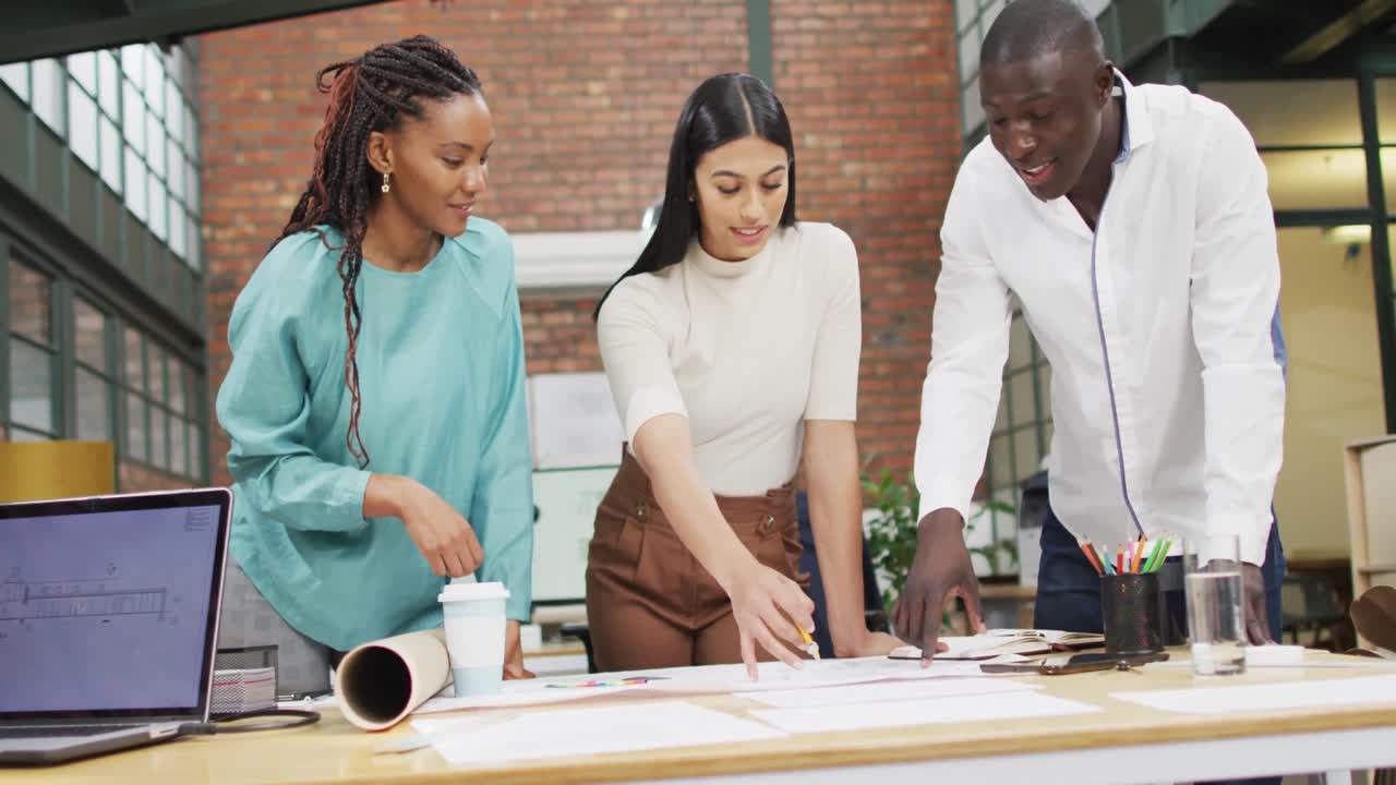 Happy diverse architects looking at architectural blueprints and discussing work at office
