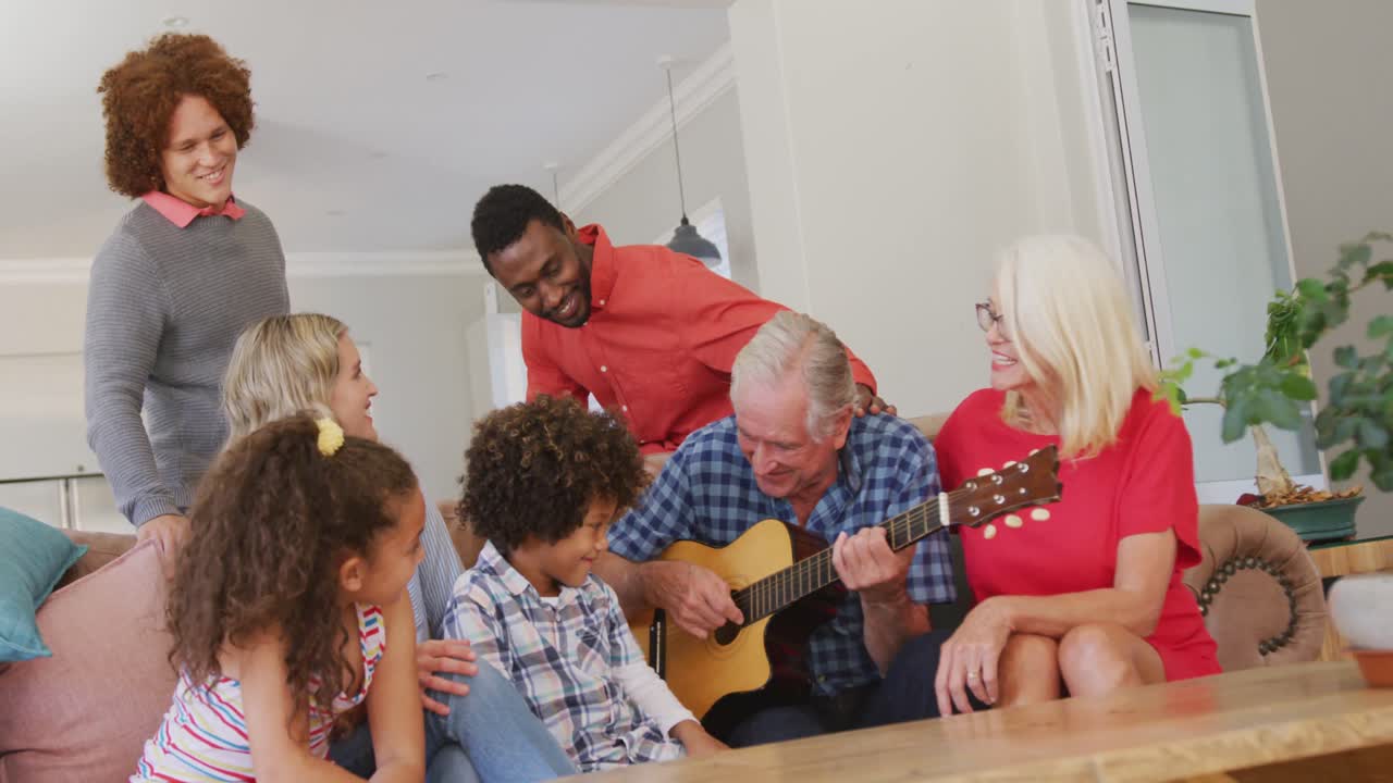 Video of diverse family siting on the couch and grandfather playing the guitar