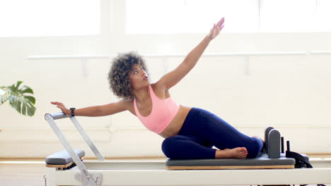 a biracial young woman with curly hair is training on pilates reformer