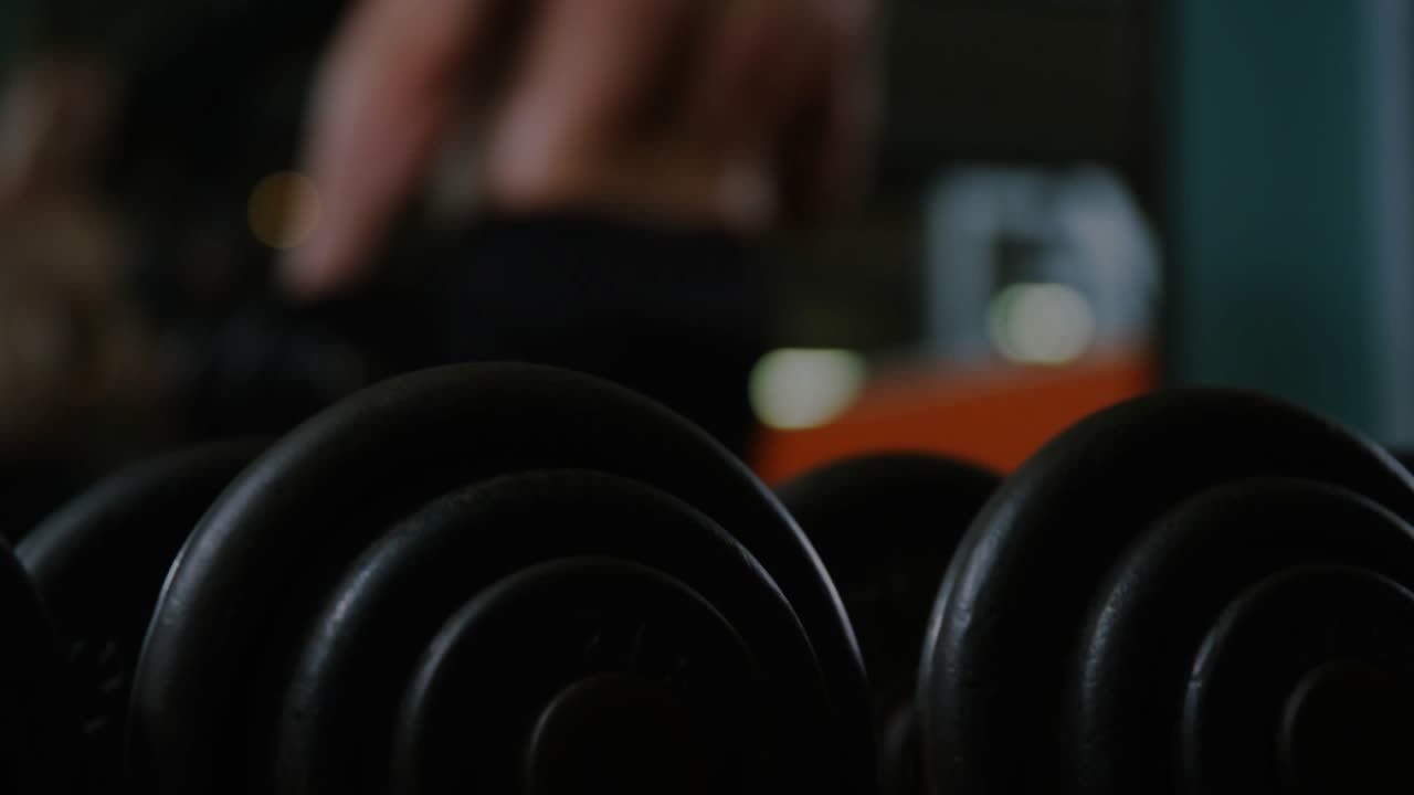 Gym lifter grabbing dumbbell causing encryption overlay across mirror while peer curling for gains