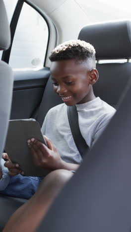 Vertical video: African American boy holding tablet, smiling in car