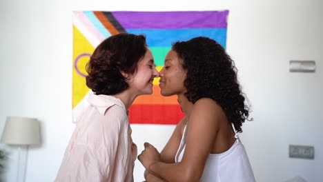 Happy-diverse-lesbian-couple-sitting-together-against-rainbow-flag