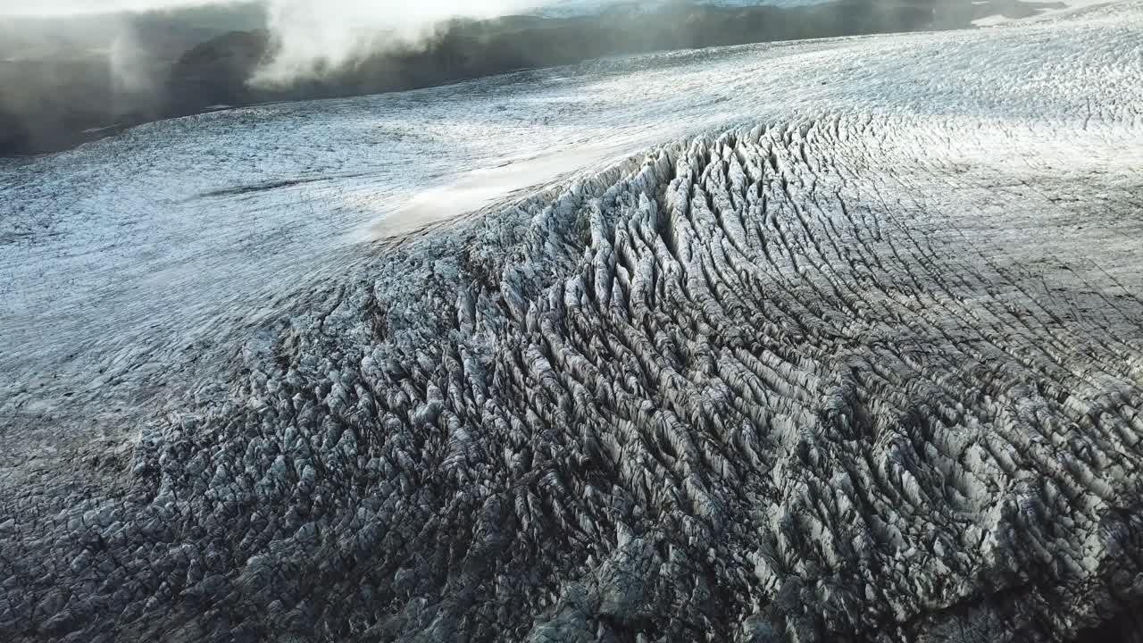 Aerial landscape view through clouds, over the textured ice surface of an icelandic glacier