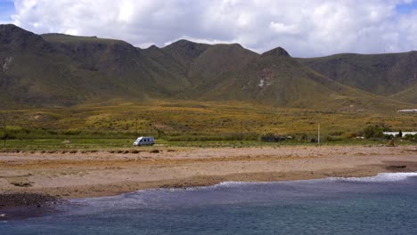 camper van in green fields near mountain and blue sea water