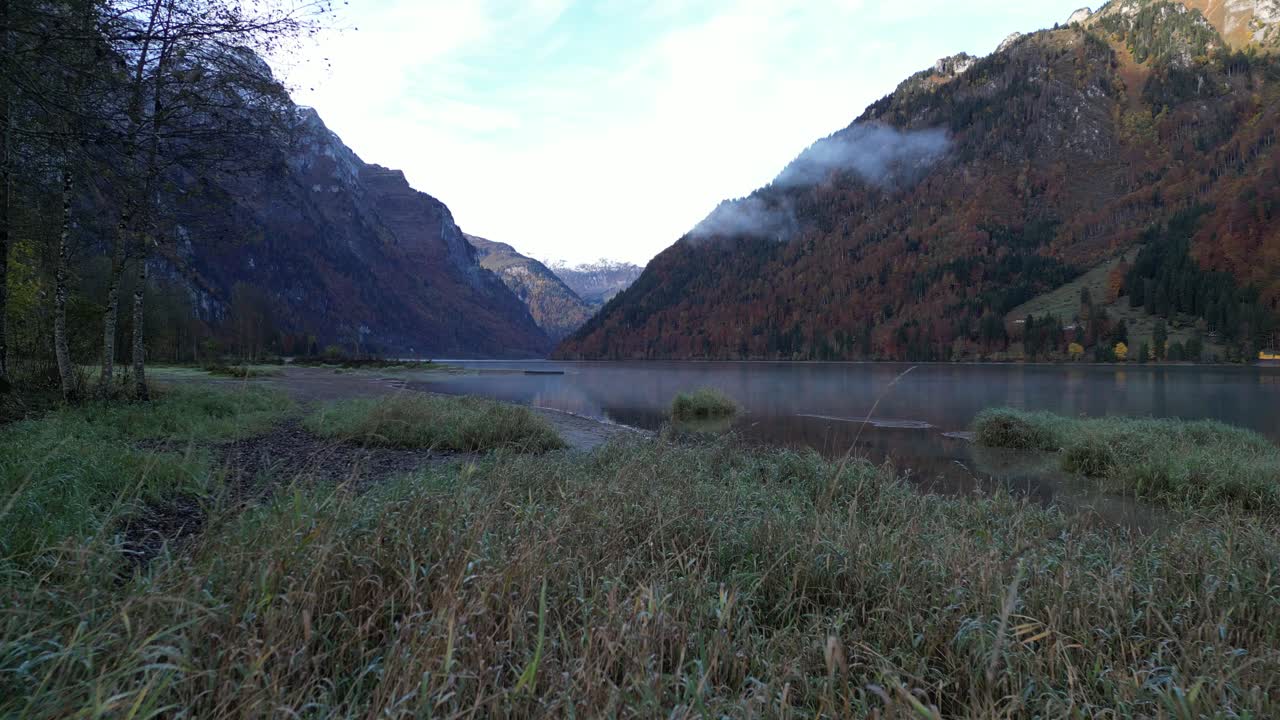 Fast zoom in shot over a lake in the valley with grass and snow mountain summit in the background