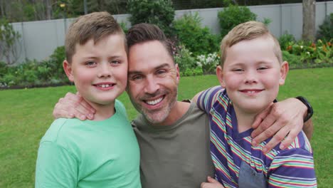 retrato de un padre caucásico y dos hijos sonriendo en el jardín