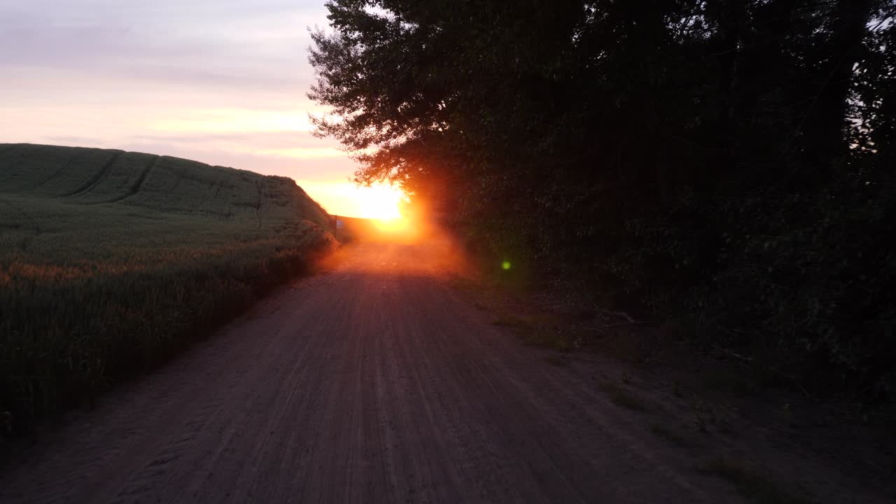 Captivating aerial footage of a serene rural landscape as the sun sets over a quiet road, casting a warm glow. The tranquil scene shows vibrant colors and a peaceful ambiance