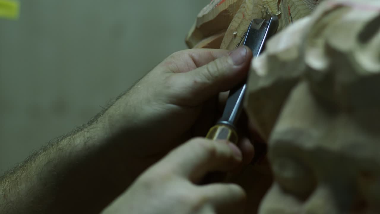 A sculptor’s steady hands guide a sharp chisel while shaping fine details into an unfinished wooden statue, capturing craftsmanship and artistry up close
