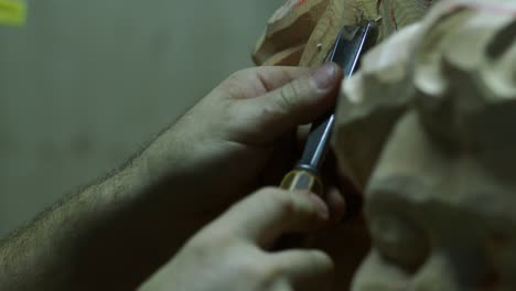 a sculptor’s steady hands guide a sharp chisel while shaping fine details into an unfinished wooden statue, capturing craftsmanship and artistry up close