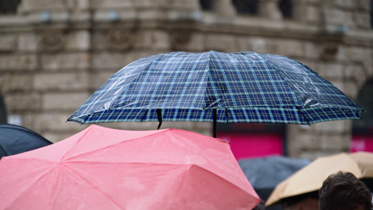 People holding umbrellas walking in the rain on thee street in Milan, Italy