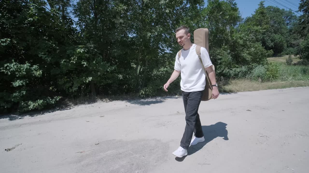 숲 근처의 거리에서 기타를 들고 는 젊은 남자