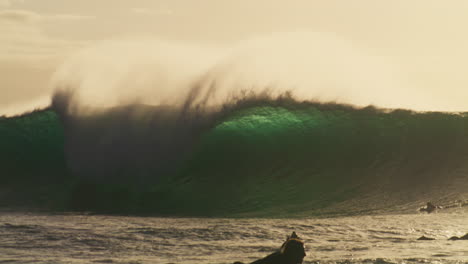 los surfistas remanan rápidamente para salir de la zona de impacto de una enorme ola reluciente.