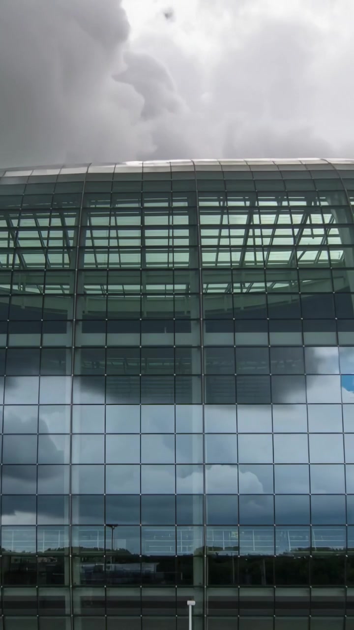 Vídeo vertical: Fachada de vidro refletora reagindo às mudanças das nuvens no campus, revelando a linha das árvores.