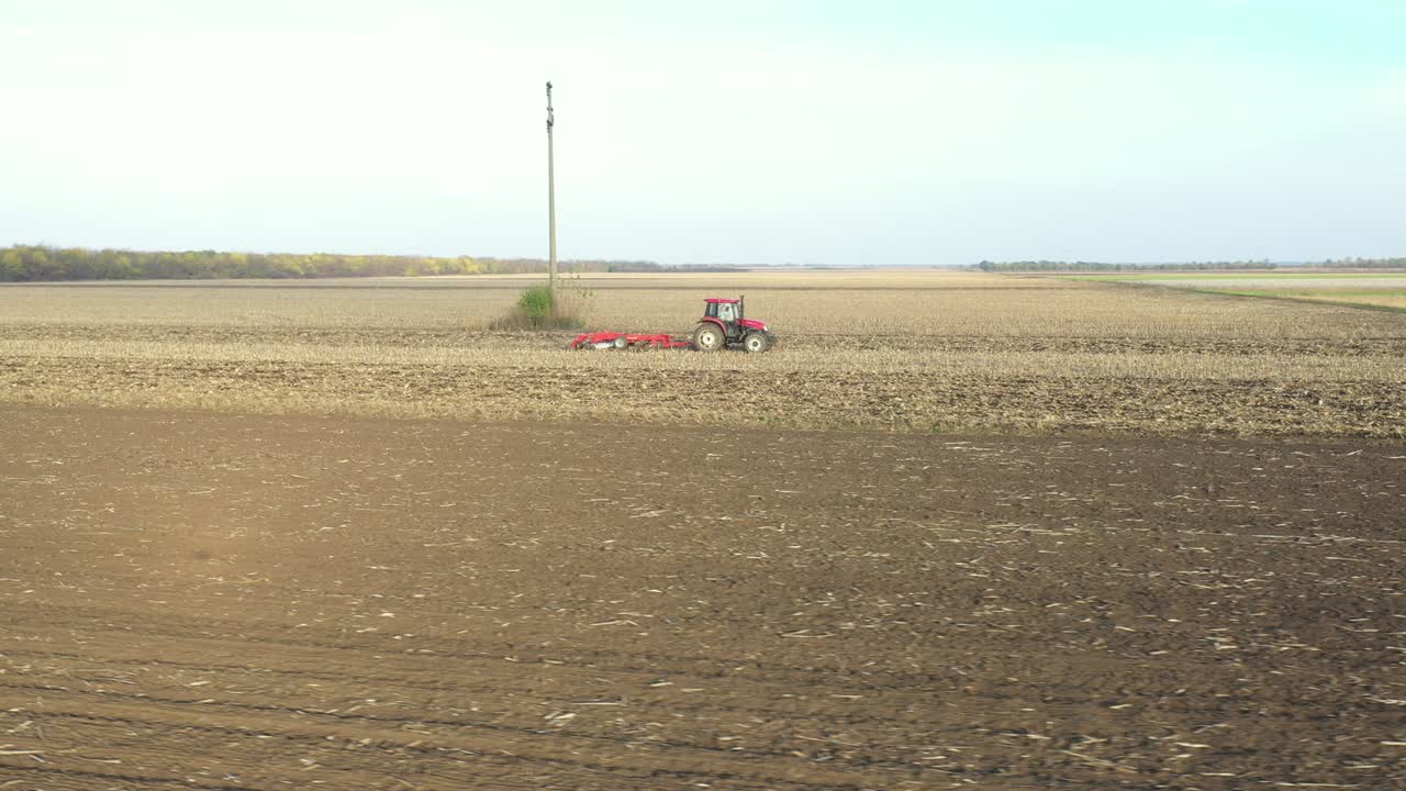 vista lateral aérea de un tractor que arrastra una harra de disco sobre un campo agrícola, tierras de cultivo