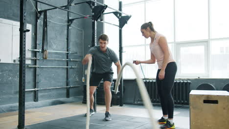 man and woman working out with battle ropes in gym
