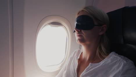 a young woman with a dark bandage in her eyes sleeps in the cabin of a passenger aircraft traveling
