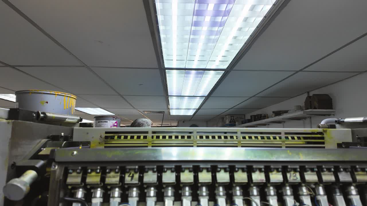 Close up Printing press. Machine with numerous spools and wires, under industrial lighting.