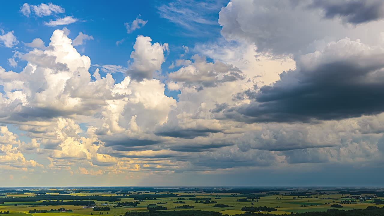 A wide panoramic shot of a stunning, changing sky with bright white and dark clouds over a vast, flat green agricultural landscape