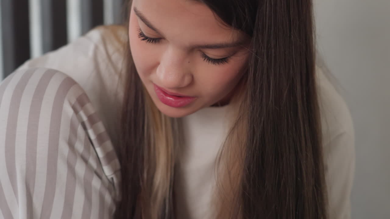 Side view focused girl with head down, concentrating on task out of frame, long straight hair, striped trousers, soft indoor light, calm mood, blurred background highlighting intent expression