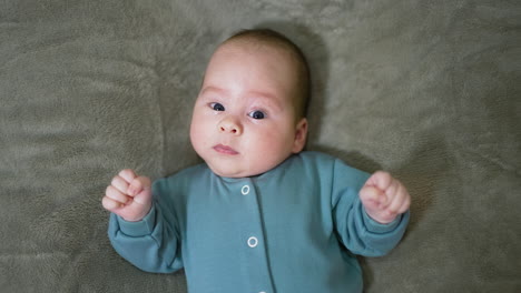 baby boy in blue sweater lies and looks straight ahead. little child watches camera with surprise and lies still. top view. close up.