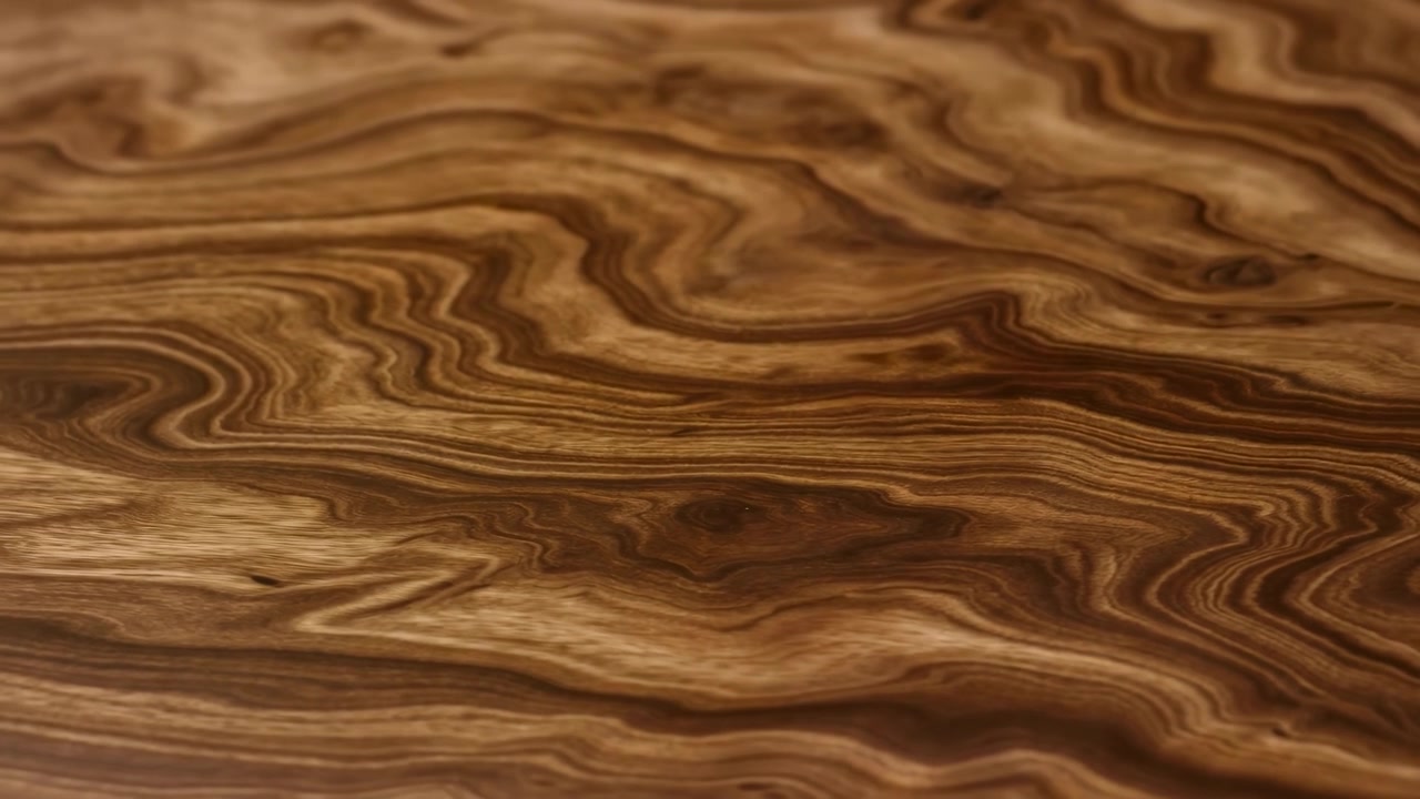 Primo piano ravvicinato di un pannello di legno lucidato che riempie l'inquadratura, mostrando ricche venature a spirale, nodi e linee ondulate in varie tonalità di marrone caldo.