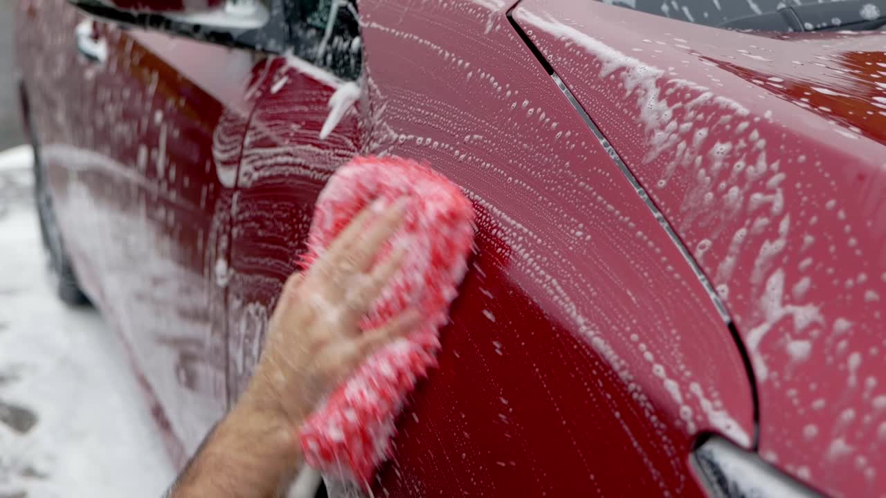 Washing a dark cherry red EV car with snow foam and shampoo with a red microfibre wash mitt - close up on fender