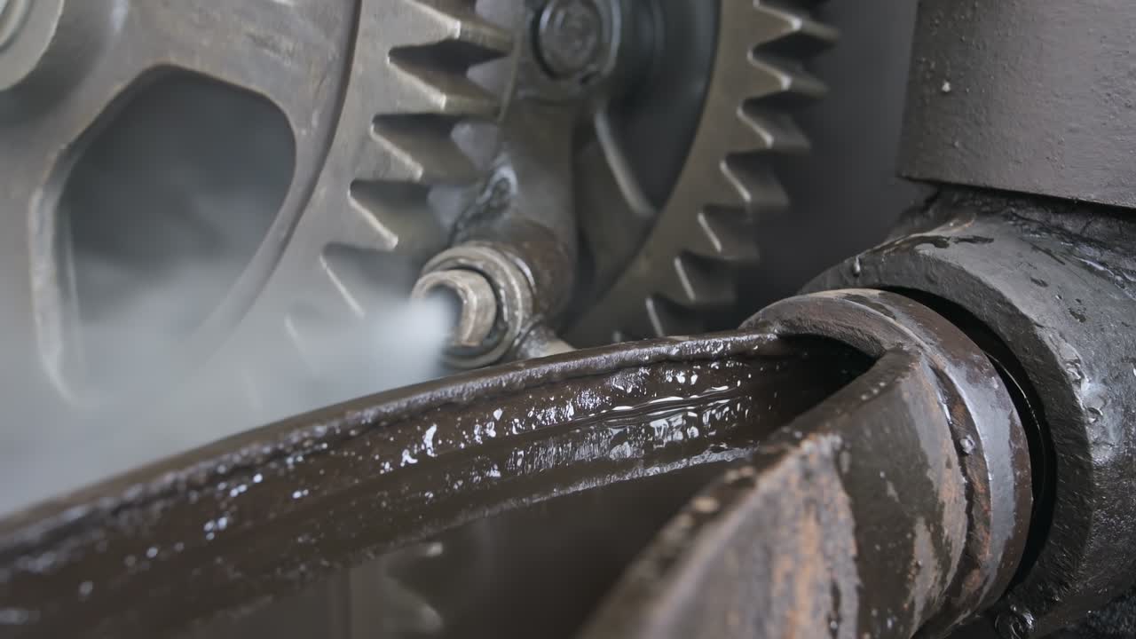 Primo piano di ingranaggi e macchinari industriali pesanti con vapore in uscita durante il funzionamento della fabbrica.
