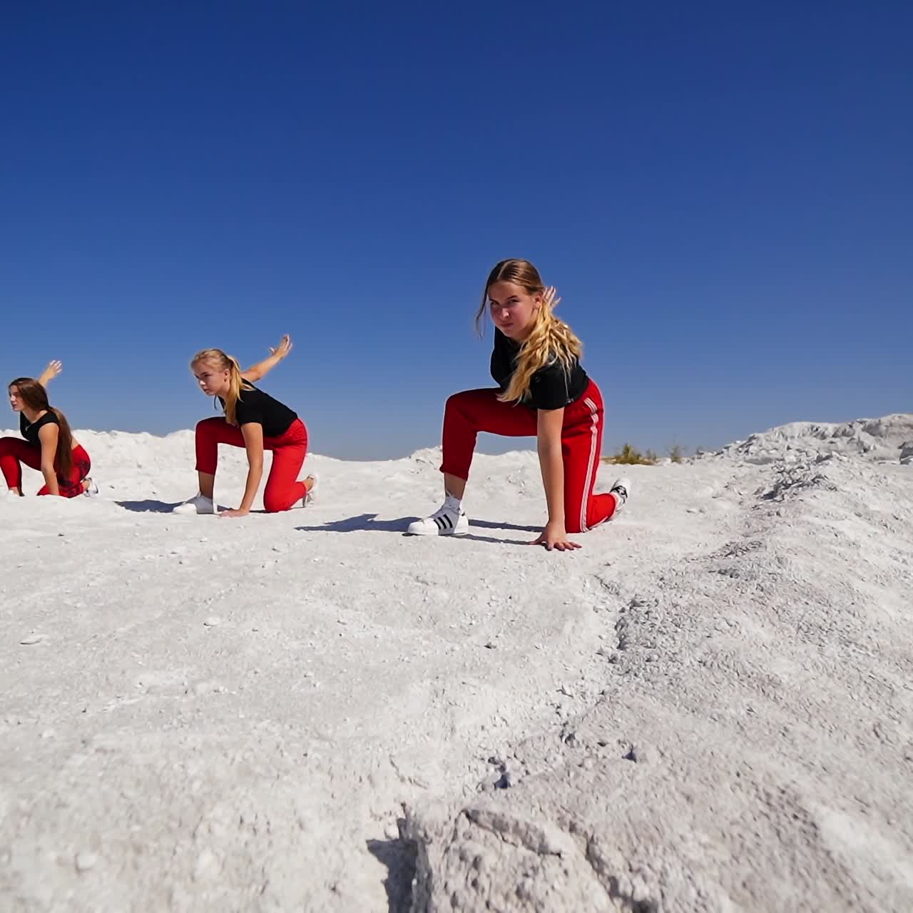 Three long-haired girls in black tops and red pants performing outdoors. Group of teenagers dancing on the rocks on sunny daytime