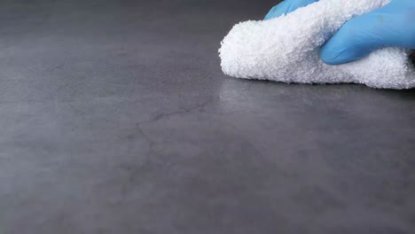 cleaning a granite countertop with a white cloth and blue gloves