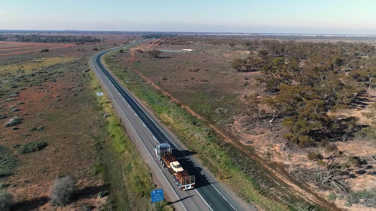 camión conduciendo por la carretera a través de campos desérticos, día soleado con cielo azul, después de toma aérea