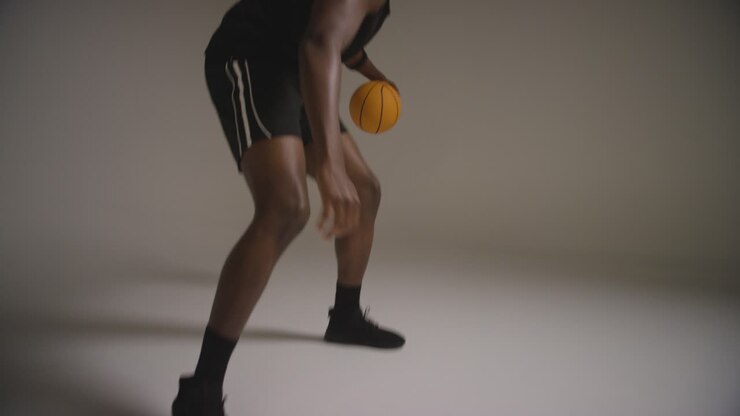 Studioaufnahme von männlichem Basketballspieler beim Dribbeln und Prellen des Balls vor weißem Hintergrund