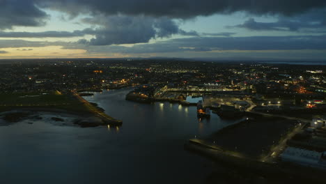 time-lapse aerial shot capturing a vast vista of galway city at twilight, filmed from the mouth of the river corrib, showcasing the city lights and dramatic sky.