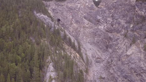 rocky mountain aerial flies up steep dry drainage to large cave mouth