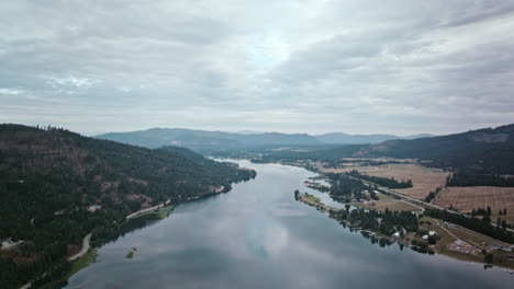 aerial video of the priest river under an overcast sky, framed by green mountains and open fields, the water stretching toward the horizon