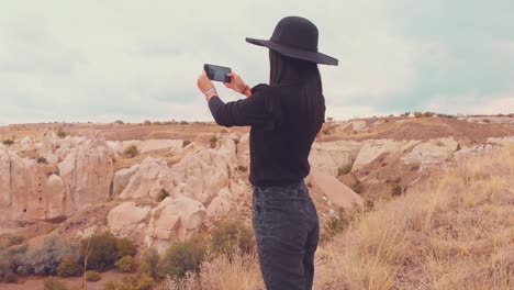 static view young caucasian female tourist in dark clothes with smart phone handheld capture holidays nature ; photo in scenic location